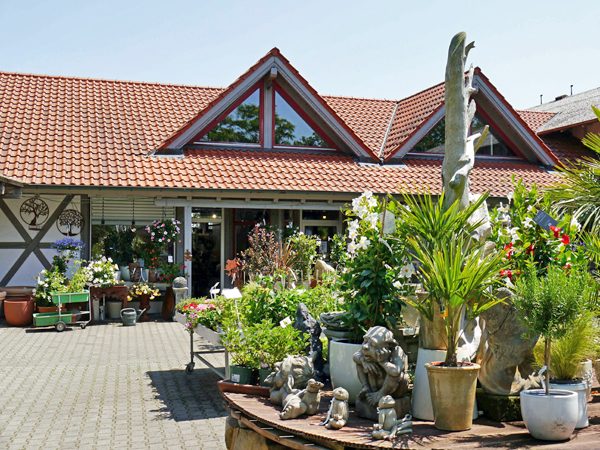 Eingang Gartencenter Blühender Pflanzen und verschiedene Skulpturen vor dem Gartencenter.